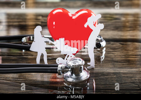 Close-up Of Family Cut Out And Red Heart With Stethoscope On Desk Stock Photo