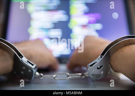 Close-up Of Person's Hand With Handcuff Using Laptop Stock Photo