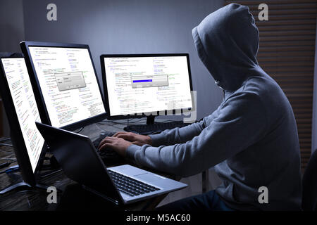 Rear View Of A Hacker Using Multiple Computers For Stealing Data On Desk Stock Photo
