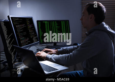 Side View Of Hacker Stealing Information From Multiple Computers On Wooden Desk Stock Photo