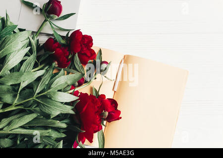 freelance concept. stylish laptop with note book and beautiful red peonies on white wooden background flat lay. space for text. top view. happy womens Stock Photo