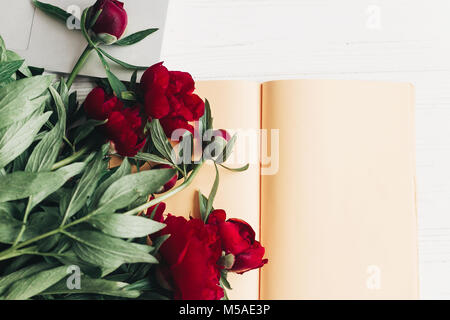 freelance concept. stylish laptop with note book and beautiful red peonies on white wooden background flat lay. space for text. top view. happy womens Stock Photo