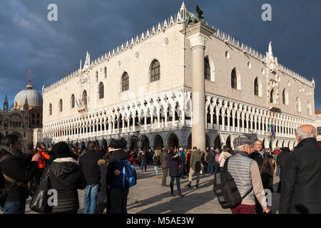 Dramatic beam of light on the Doges Palace, Venice, Italy as a storm approaches with ominous grey cloud and tourists in the foreground in Piazzetta Sa Stock Photo