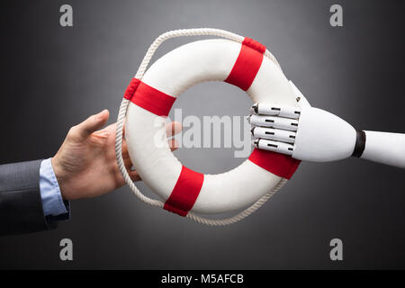 Robot Giving Lifebelt To Businessperson Over Gray Background Stock Photo