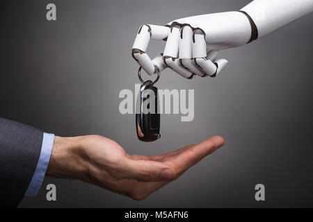 Close-up Of A Robot Giving Car Key To Businessperson On Grey Background Stock Photo