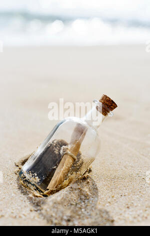 closeup of a glass bottle with a rolled message inside stranded in the sand of a lonely beach, with some blank space on top Stock Photo