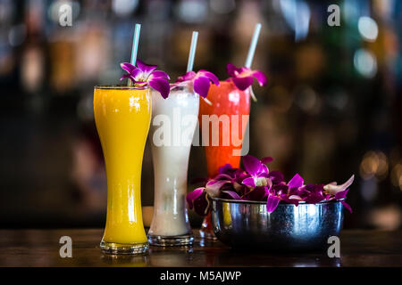 Vertical  composition with 3 yellow, white, red cocktails and orchid flowers on the blurred background Stock Photo