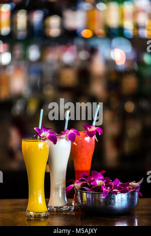 Vertical  composition with 3 yellow, white, red cocktails and orchid flowers on the blurred background Stock Photo