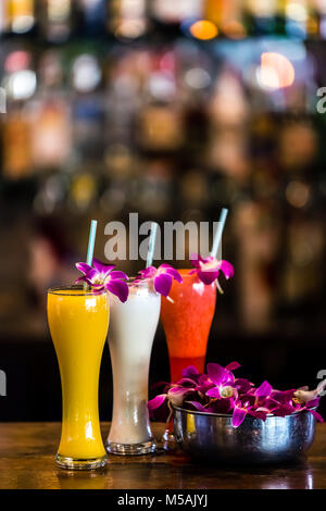 Vertical  composition with 3 yellow, white, red cocktails and orchid flowers on the blurred background Stock Photo