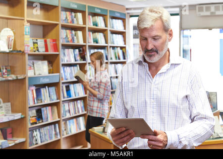 Male Bookstore Owner Using Digital Tablet With Customer In Background Stock Photo