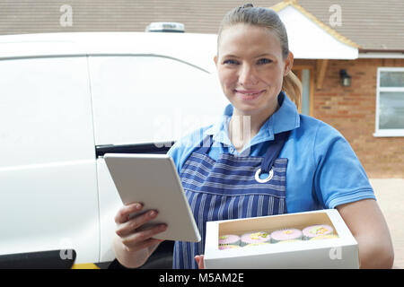 Portrait Of Female Baker With Digital Tablet Making Home Delivery Of Cupcakes Stock Photo
