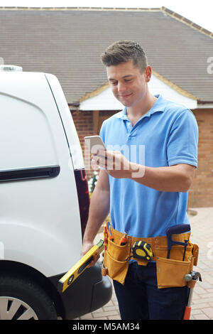 Builder With Van Checking Text Messages On Mobile Phone Outside House Stock Photo