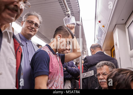 Tehran, Iran - April 29, 2017: Iranian men of different ages ride the subway, one of them listens to music on headphones, another stands and smiles. Stock Photo