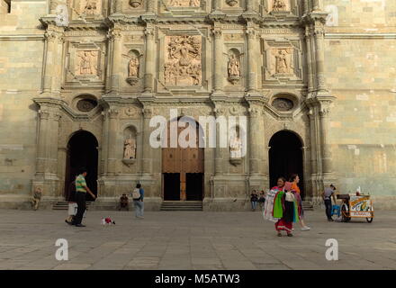 People individually making their way through the day as their paths cross in front of the iconic Cathedral of Our Lady of the Assumption in Oaxaca. Stock Photo