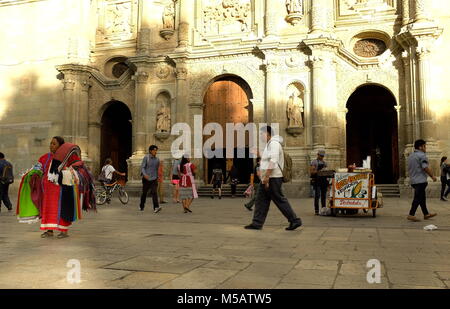 People individually making their way through the day as their paths cross in front of the iconic Cathedral of Our Lady of the Assumption in Oaxaca. Stock Photo