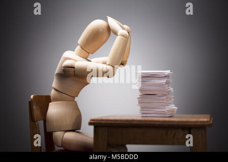Wooden Dummy Figure Suffering From Headache Sitting On Chair With Stack Of Documents On Desk Stock Photo