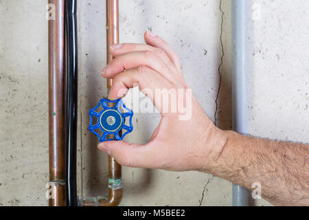 Male hand turning blue valve on copper pipe Stock Photo