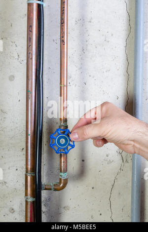 Man gently turning a valve on a water pipe to control the flow using his fingertips in a basement utility room in a close up view of his hand Stock Photo
