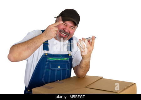 Laughing happy male worker in denim overalls leaning on a cardboard box talking on a speaker phone and gesturing with his hand isolated on white Stock Photo