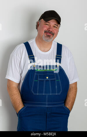 Portrait of cheerful man wearing dungarees standing against white wall Stock Photo