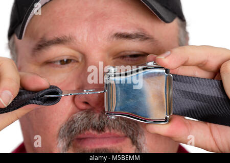 Stupid dim-witted man unable to fasten a seatbelt or perform the most simple task holding the buckle and clip in front of his face as he tries to solv Stock Photo