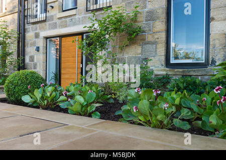 Small corner of beautiful, landscaped, private garden with contemporary design, paved patio, border shrubs & plants by house - Yorkshire, England, UK. Stock Photo