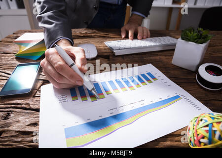 Close-up Of A Businessperson's Hand Analyzing Financial Graph On Wooden Desk Stock Photo