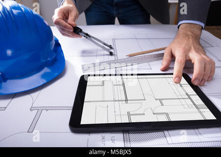Close-up Of Architect's Hand Using Digital Tablet With Blueprint On Desk Stock Photo
