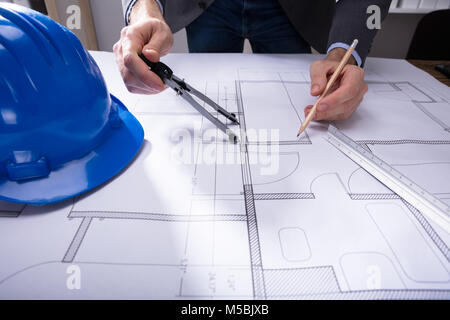 Close-up Of Architecture's Hand Working On Blueprint With Hardhat On Desk Stock Photo