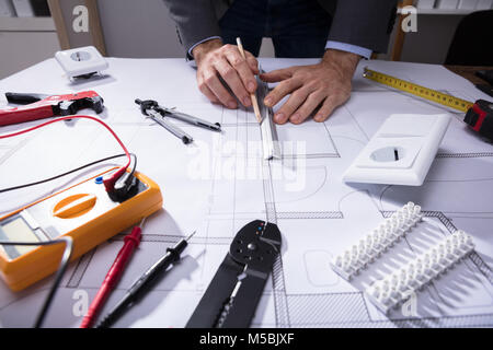 Architect Using Pencil To Draw Blueprint Besides Tools And Digital Multimeter Stock Photo