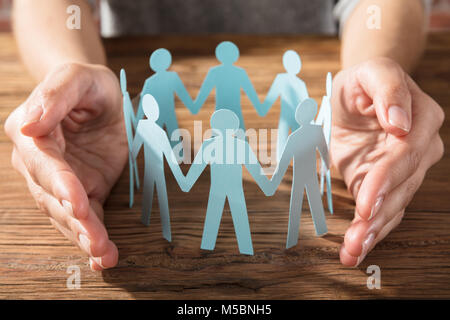 Close-up Of A Person Protecting Paper Cut Out Figure On Wooden Desk Stock Photo
