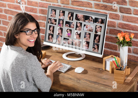 Smiling Young Female Designer Working At Workplace With Set Of Models On Computer Screen Stock Photo