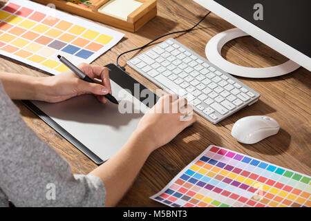 Graphic Designer Using Graphic Tablet With Color Samples On Desk Stock Photo