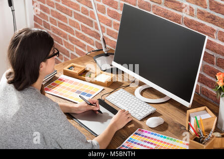 Young Female Graphic Designer Using Graphic Tablet With Color Samples On Desk