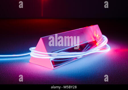 A Studio Still-life Photograph of a Triangular Glass Prism with Abstract Neon Lighting in Blue-Grey, and Red Laser Light Entering the End of the Prism Stock Photo