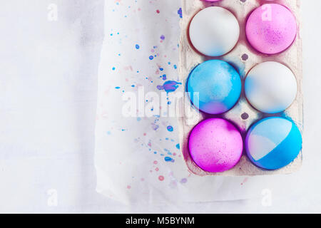 Easter eggs painted in blue and pink shades in a carton with drops of dye. Modern Easter concept with copy space. Concrete background from above. Stock Photo