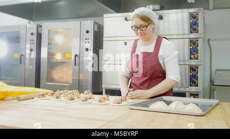 Adult woman in glasses bakes cakes in the bakery Stock Photo