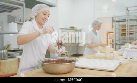 Baker mixes chocolate cream in metal bowl and making cakes Stock Photo