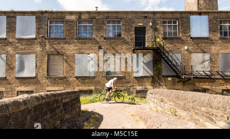 Leeds, England - June 30, 2015: A cyclist rides past old factory buildings on the towpath alongside the Leeds and Liverpool Canal in West Yorkshire. Stock Photo