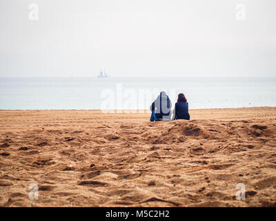 Сouple of lovers sitting on the beach with a sailing ship on the horizon Stock Photo