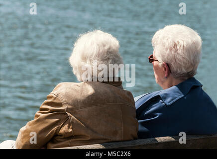 older women sitting on a wooden bench near the water Stock Photo
