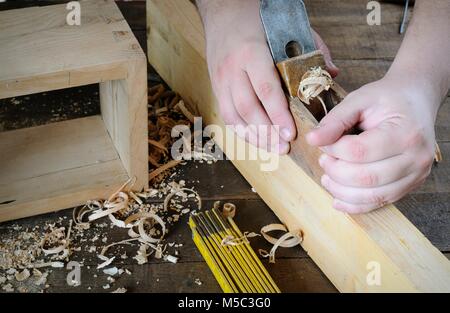 Man's hands working with plane on wood plank. Unrecognizable. Stock Photo