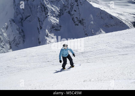 Snowboarder downhill on ski slope in high snowy mountains at sun winter day. Caucasus Mountains, region Dombay. View from above. Stock Photo