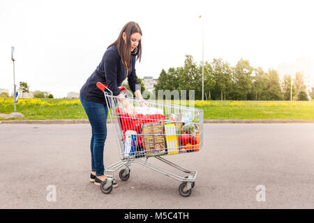 Pretty teenager in blue clothes organizes her shopping basket trolley Stock Photo