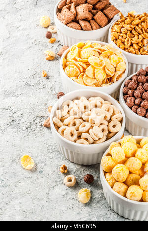 Set of various breakfast cereal corn flakes, puffs, pops, grey stone table copy space Stock Photo