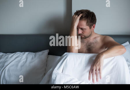 Portrait of an upset young man sitting on a bed alone. Stock Photo