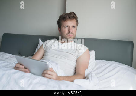 attractive caucasian young man using tablet in bed in the morning Stock Photo