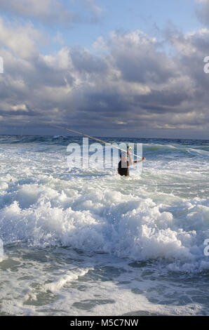Surf fisherman into the waves. Fishing scene. surf casting. Stock Photo