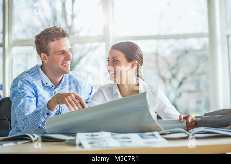 Smiling young architects discussing over blueprint at office desk Stock Photo
