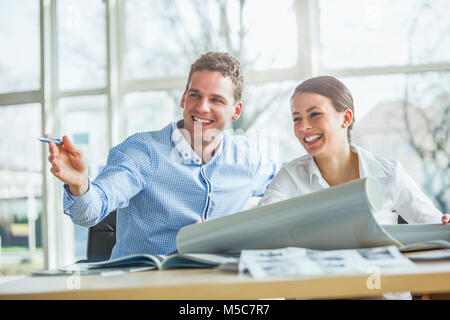 Smiling young architects looking away while discussing over blueprint at office desk Stock Photo